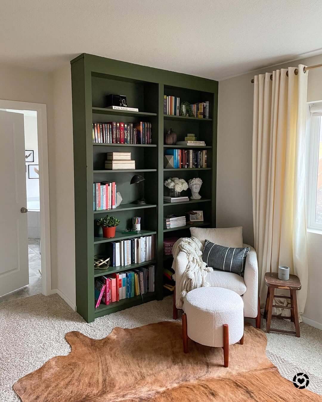 Green Bookcase With Sculptural Busts and White Flowers