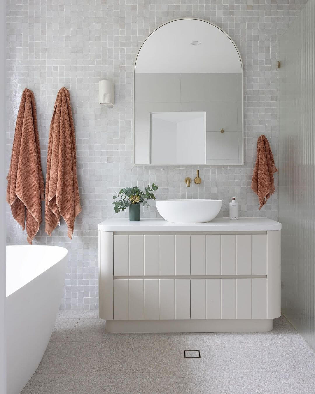 Arched Mirror Frames a Softly Tiled Vanity Wall