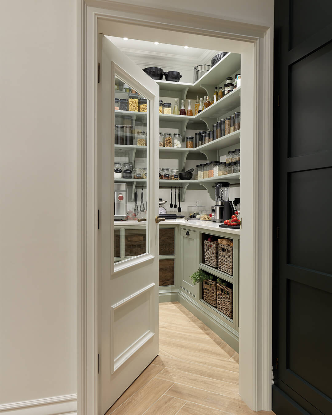 Sage green cabinets and woven baskets add natural texture to pantry storage