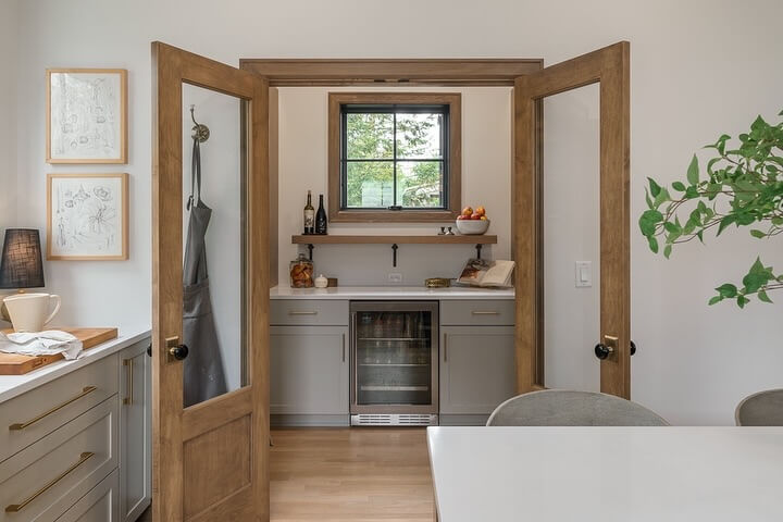 Glass-paneled doors with dark knobs offer a peek into the pantry