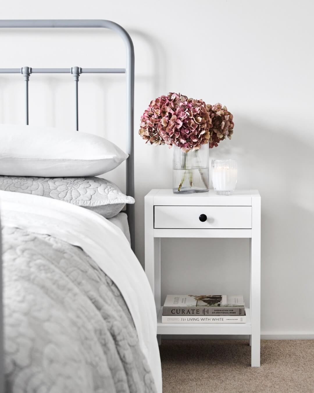 White Bedside Table Holds Books and Flowers