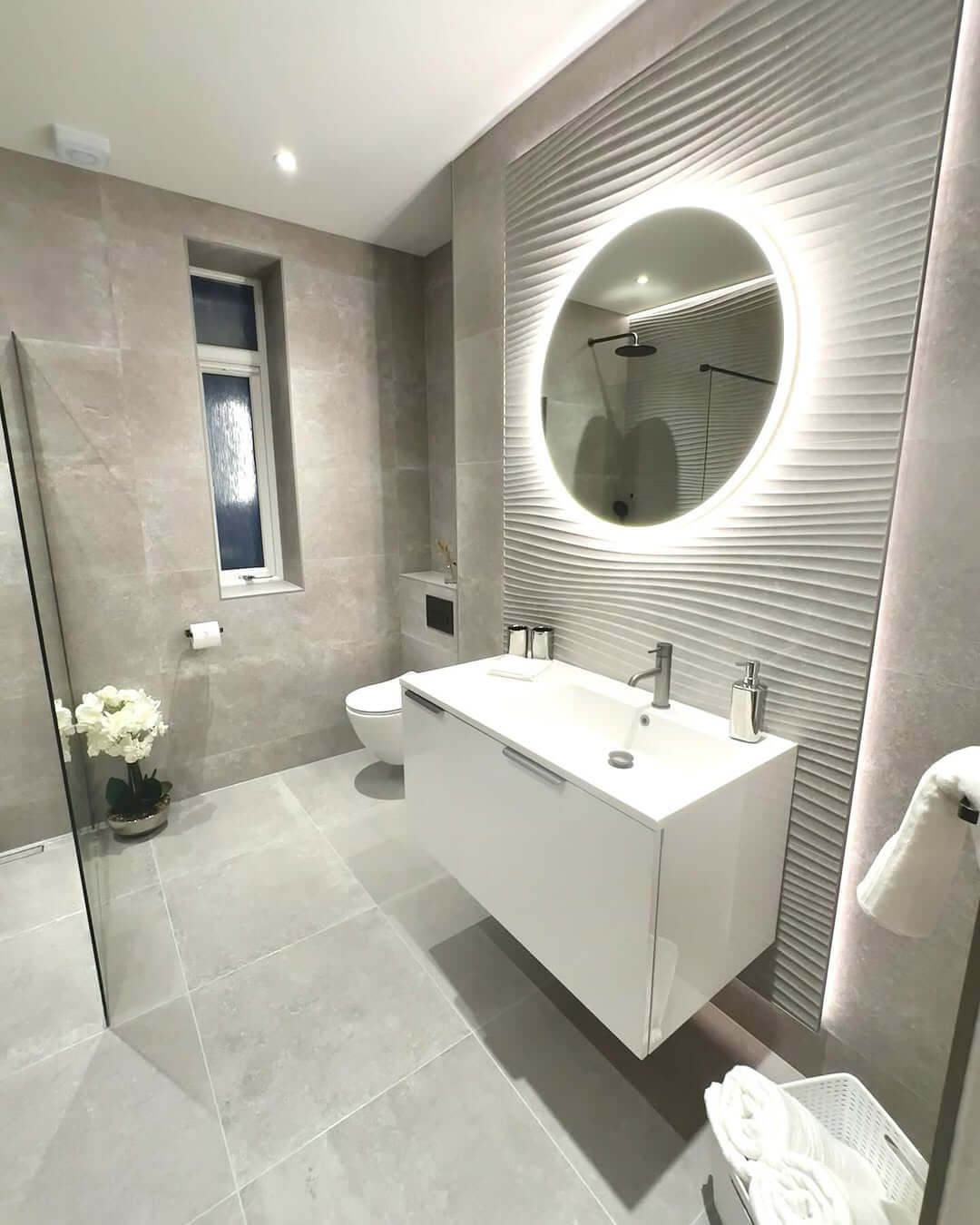 Textured Wall Panels Frame a Round Illuminated Mirror