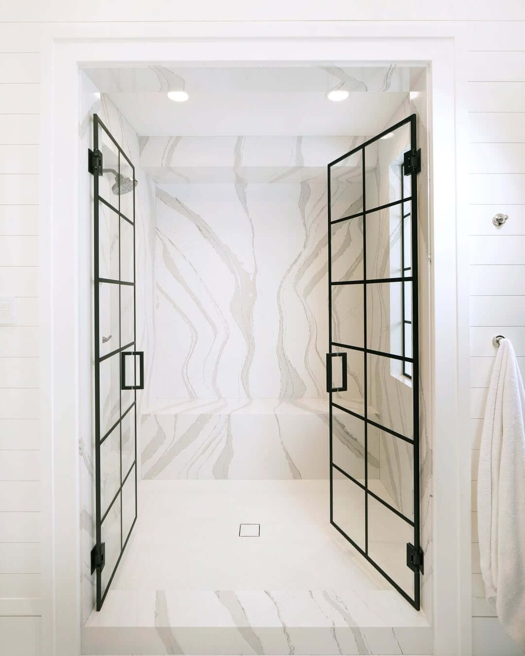 Black Grid Shower Doors Frame a Marble-Veined Enclosure