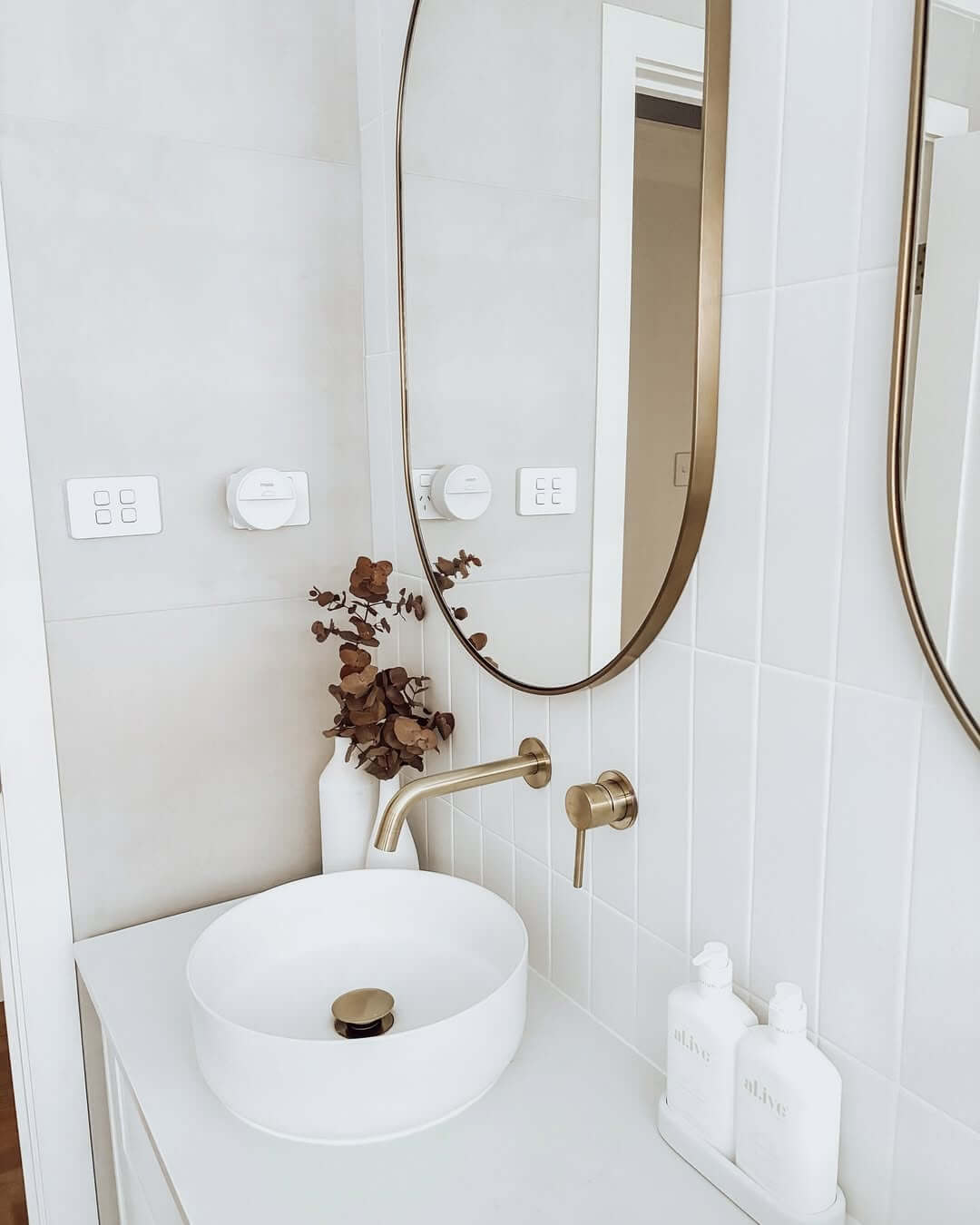 Oval Mirror with Thin Gold Frame Above a White Vessel Sink